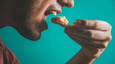 volto di uomo con una mano che avvicina del cibo alla bocca 