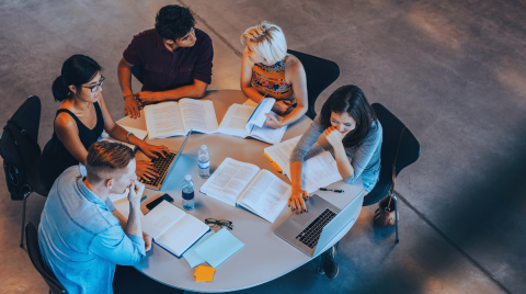 ragazzi e ragazze attorno a un tavolo che studiano, leggono e scrivono