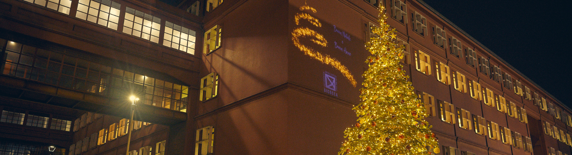 albero di Natale e proiezione scritta auguri di Buone feste su edificio Università Bicocca