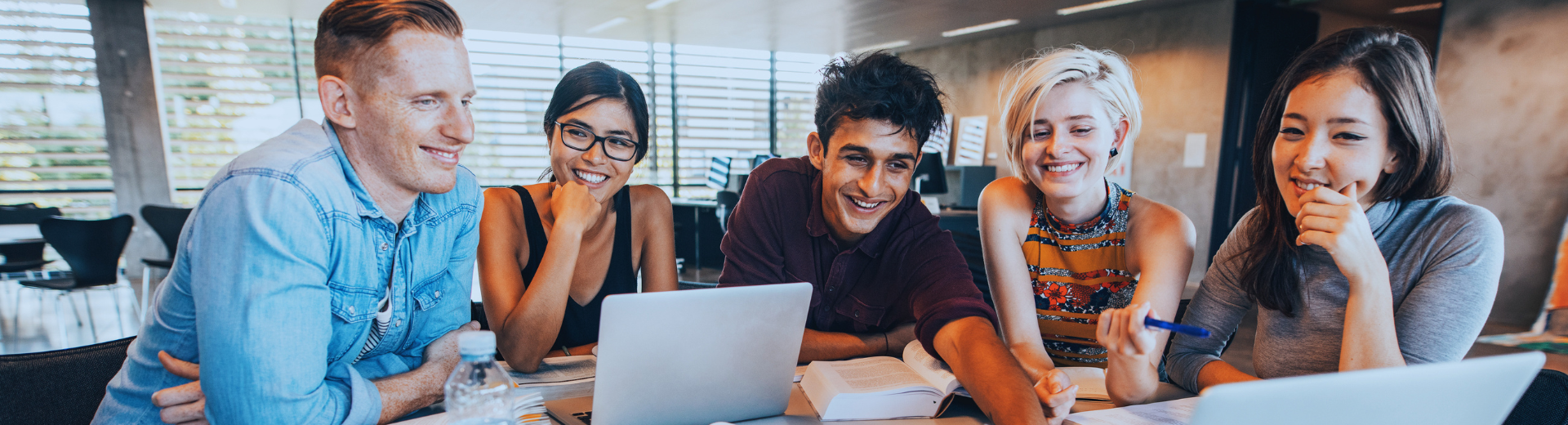 studenti universitari sorridenti davanti a pc seduti attorno a un tavolo